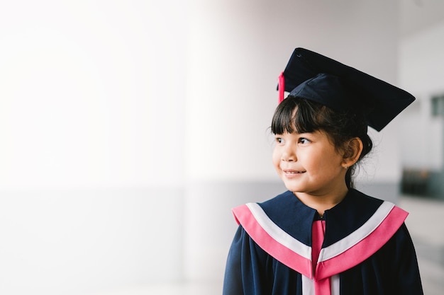 Portret van een schattig aziatisch afgestudeerd schoolmeisje met afstudeerjurk op school