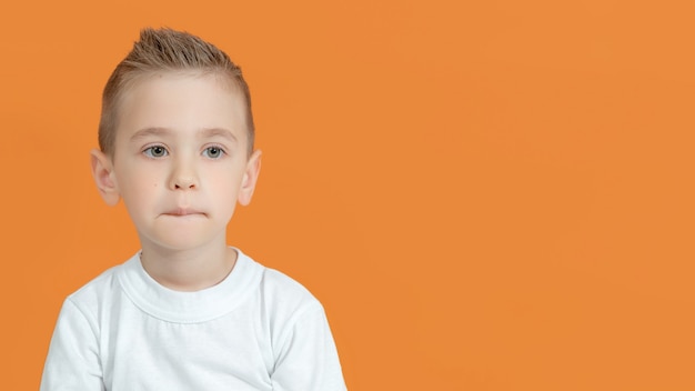 Portret van een schattig broeiend kind met een samengeknepen lip, een serieuze jongen staat voor de camera te denken