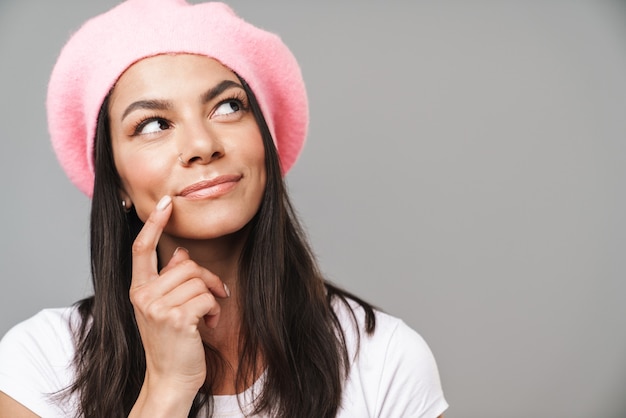 Portret van een schattig denkende dromende jonge Franse vrouw in baret poseren geïsoleerd over grijze muur.