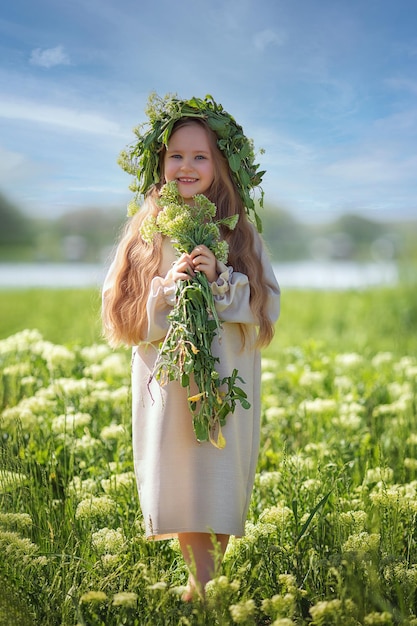 Portret van een schattig dorpsmeisje in een krans op een bloemenveld Een kind in een bloeiende weide