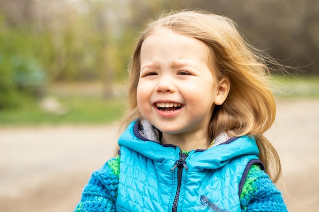 Portret van een schattig gelukkig klein blond meisje in een blauwe jas in het voorjaar