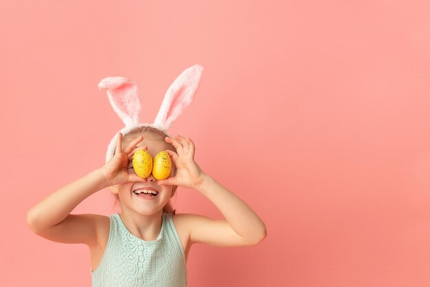 Foto portret van een schattig glimlachend meisje met konijnenoren en gele paaseieren die de ogen sluit