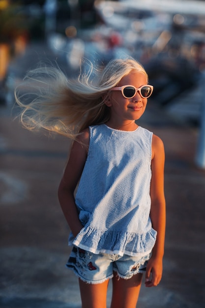 Portret van een schattig glimlachend tien-jarig meisje met bril. Een meisje in korte broek en een blauw t-shirt bij zonsondergang in de buurt van de zee. Turkije.