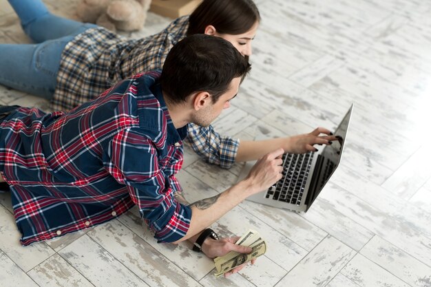 Portret van een schattig jong stel dat thuis op de vloer ligt en het budget beheert met behulp van een laptop