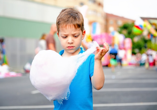 Portret van een schattig kind dat suikerspin eet op een achtergrond van een zomers eerlijk festival