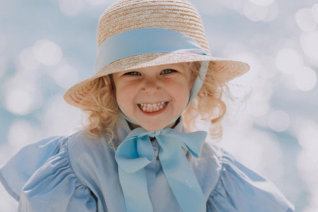 portret van een schattig klein blond meisje in blauwe jurk en strohoed buitenshuis