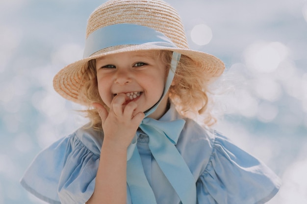 portret van een schattig klein blond meisje in blauwe jurk en strohoed buitenshuis