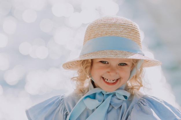 portret van een schattig klein blond meisje in blauwe jurk en strohoed buitenshuis