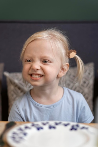 Portret van een schattig klein blond meisje met twee staarten in café Driejarig meisje glimlacht en rimpelde haar neus Wachtend op de maaltijd