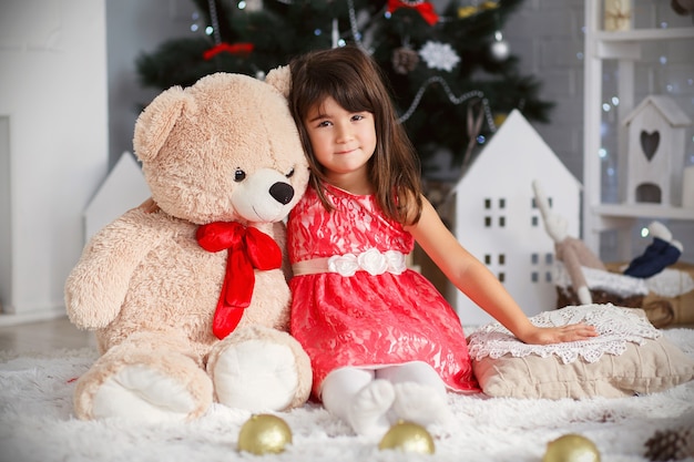 Portret van een schattig klein brunette meisje knuffelen een zachte teddybeer in interieur met kerstversiering