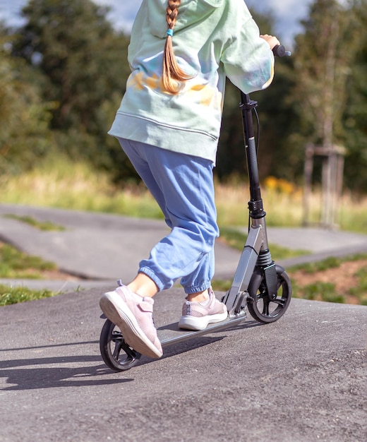 Portret van een schattig klein caucasisch schoolmeisje dat een helm draagt, geniet van het plezier van het rijden op een scooter op geasfalteerde trackxAin straatpark buitenshuis op zonnige dag Gezonde sportactiviteiten voor kinderen buiten