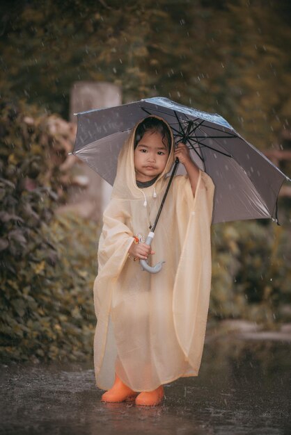 Portret van een schattig klein meisje dat een regenjas draagt en een paraplu vasthoudt op de regenende mensen in Thailand