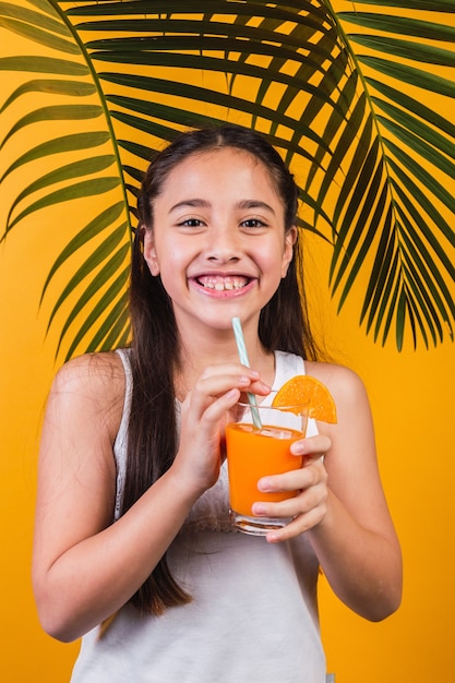 Portret van een schattig klein meisje dat geniet van sinaasappelsap op een gele achtergrond.