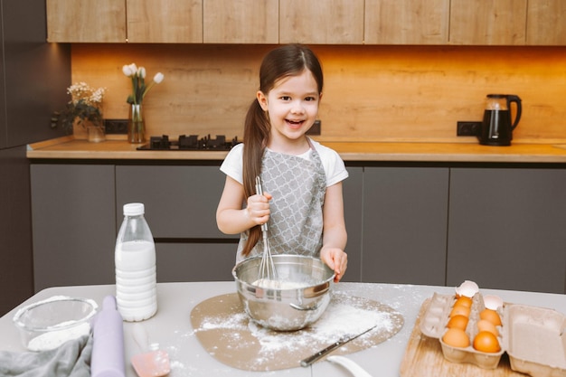 Portret van een schattig klein meisje dat in een moderne keuken staat en deeg bereidt