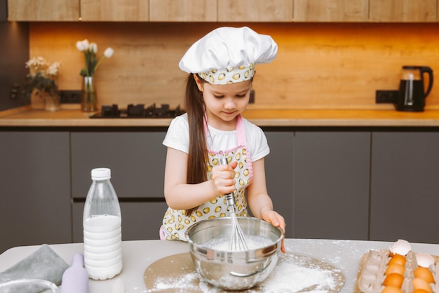 Portret van een schattig klein meisje dat in een moderne keuken staat en deeg bereidt