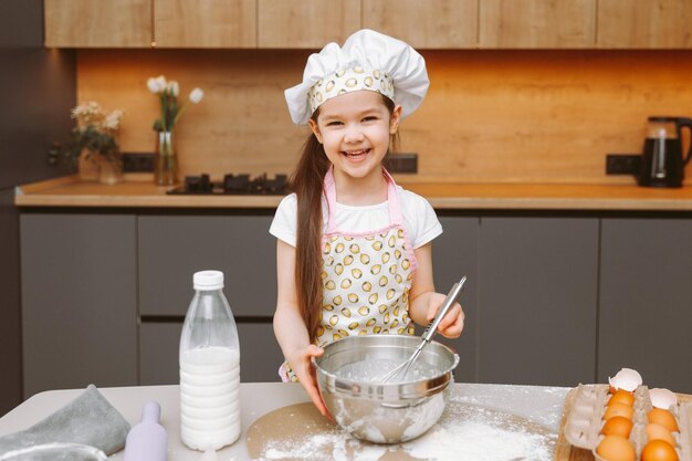 Portret van een schattig klein meisje dat in een moderne keuken staat en deeg bereidt