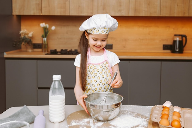 Portret van een schattig klein meisje dat in een moderne keuken staat en deeg bereidt