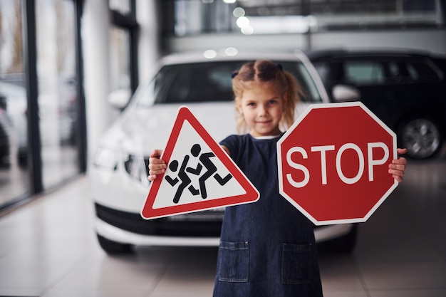 Portret van een schattig klein meisje dat verkeersborden in handen houdt in de autosalon.