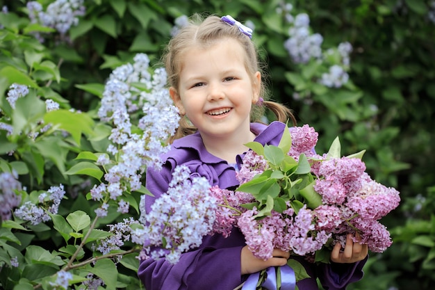 Foto portret van een schattig klein meisje in een paarse jas met een boeket seringen in haar handen
