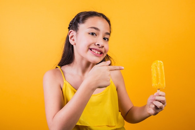 Portret van een schattig klein meisje met een gele ijslolly op een gele achtergrond.