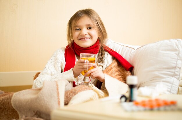 Portret van een schattig lachend meisje dat in bed zit en hete thee drinkt