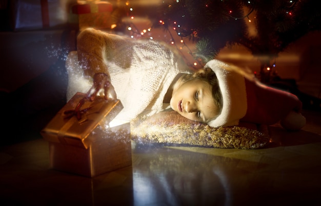 Portret van een schattig lachend meisje dat op de vloer ligt en naar de binnenkant van de magische gloeiende doos kijkt