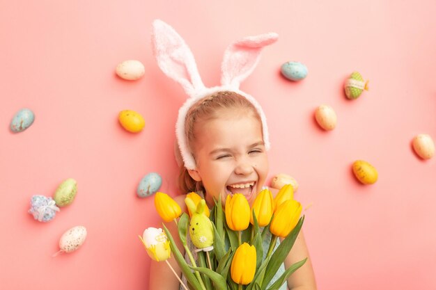 Portret van een schattig lachend meisje met konijnenoren en paaseieren houdt een lenteboeket van tulpen vast