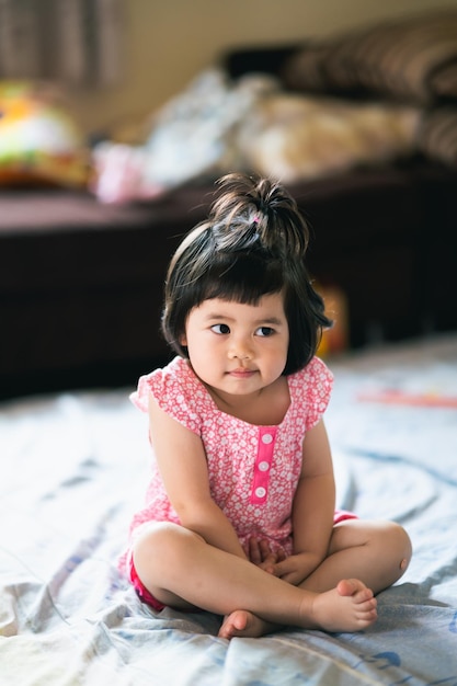 Foto portret van een schattig meisje dat op het bed zit