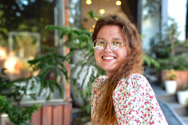 Portret van een schattig meisje met een bril in een gezellig groen café glimlacht, ontspant en kijkt naar de camera