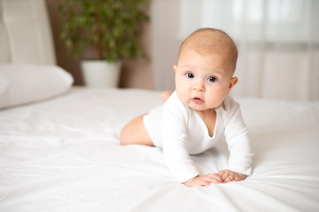 Portret van een schattig meisje van 5 maanden in een wit rompertje op een wit bed Ruimte voor tekst Kind