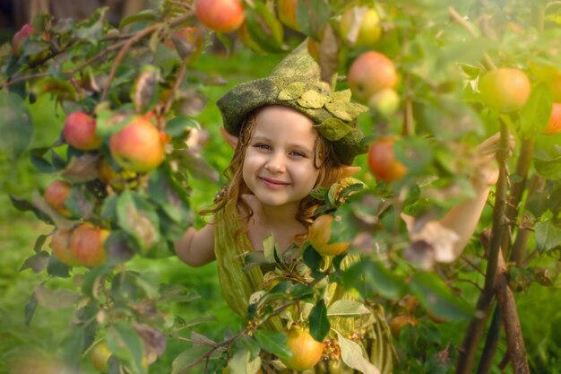 Portret van een schattig mooi meisje in een groene kabouterhoed in een boom met appels.