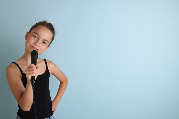 Portret van een schattig tienermeisje dat zingt met microfoon Tienermeisje in zwart t-shirt op een geïsoleerde blauwe achtergrond Karaoke voor kinderen home entertainment voor kinderen Zangeres zingt met microfoon