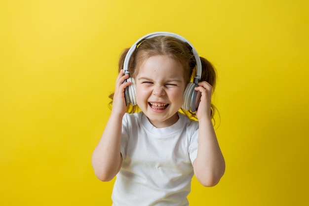 Portret van een schattig vrolijk meisje dat naar muziek luistert met een witte koptelefoon. audioboeken, audiolessen. onderwijsconcept. fotostudio, gele achtergrond, tekstruimte. Hoge kwaliteit foto