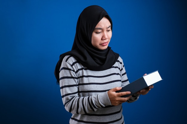 Portret van een schattige aziatische moslimvrouw die ziek en moe is en te veel boeken leest over een blauwe achtergrond