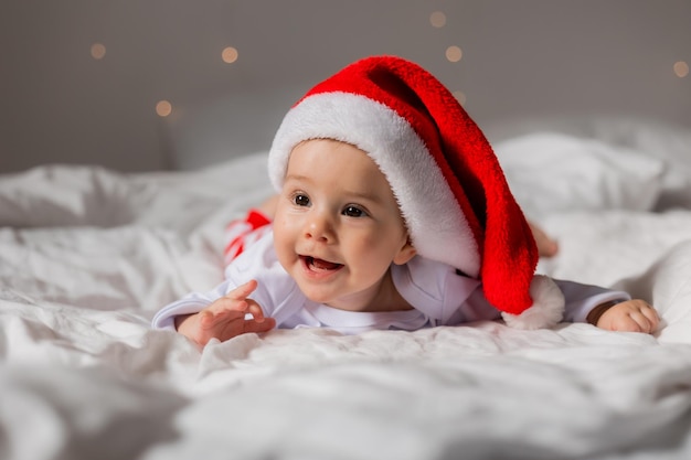 Portret van een schattige baby in een kerstman hoed glimlachend in bed thuis kerstmorgen foto van hoge kwaliteit