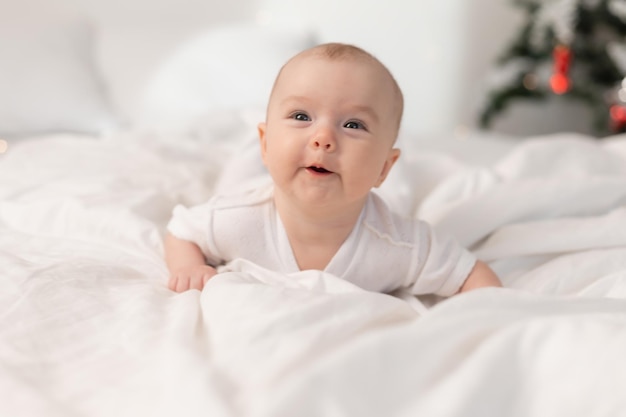 Foto portret van een schattige baby in een witte bodysuit op een bed thuis met wit linnengoed. pasgeboren baby thuis