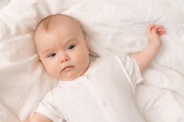 portret van een schattige baby in een witte bodysuit op een bed thuis met wit linnengoed. Pasgeboren baby thuis
