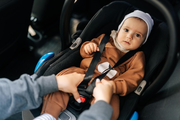Portret van een schattige baby jongen die niet herkenbaar is jonge moeder die veiligheidsgordel vastzet in de auto