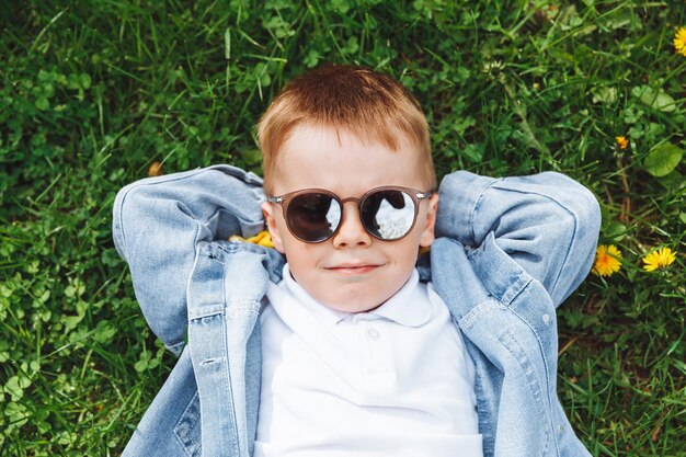 Portret van een schattige baby van 4 jaar oud Glimlachend liggend op het gras, handen onder zijn hoofd Uitzicht van bovenaf Kaukasische lente