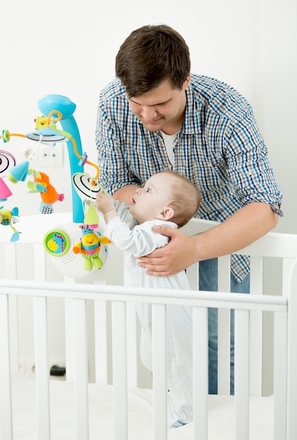 Portret van een schattige babyjongen die met zijn vader in een bedje speelt