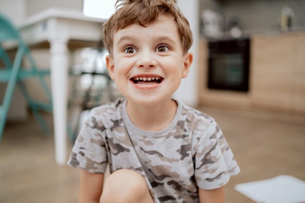 Portret van een schattige, gelukkige schoolgaande jongen die grappige gezichten trekt en naar de camera kijkt