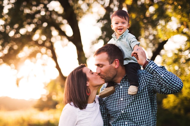 Foto portret van een schattige glimlachende baby jongen terwijl ouders elkaar kussen in het park