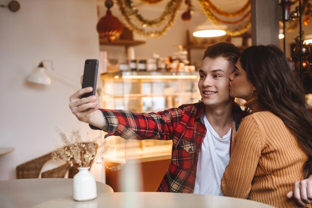 portret van een schattige jonge verliefde paar zitten in café binnenshuis een selfie maken via de mobiele telefoon.