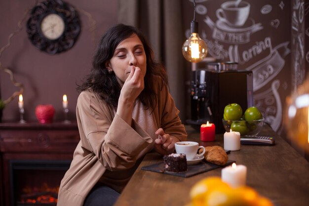 Portret van een schattige jonge vrouw die geniet van een smakelijke cake in een coffeeshop aan de toog. Vrolijke jonge vrouw die cake eet in een hipster-koffiebar.