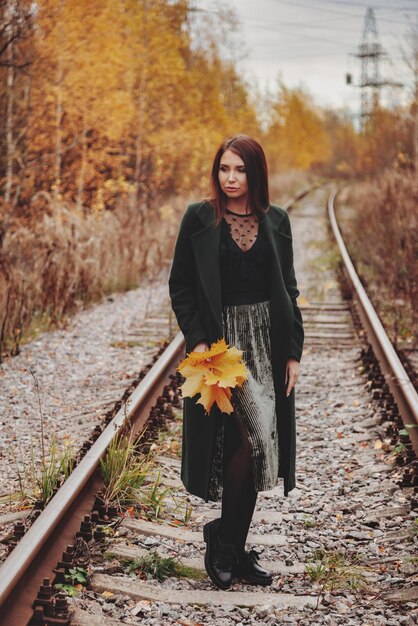 Portret van een schattige jonge vrouw met een Slavisch uiterlijk in vrijetijdskleding in de herfst, op de spoorweg tegen de achtergrond van een herfstpark en een rivier. Mooie vrouw wandelen in het bos in gouden herfst. Ruimte kopiëren