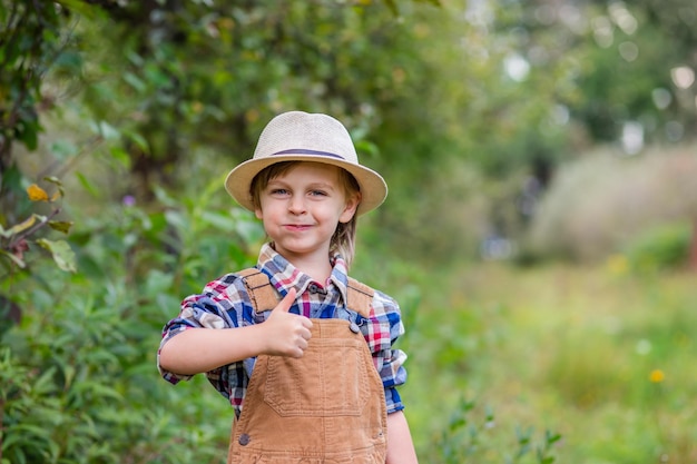 Portret van een schattige jongen in een hoed in de tuin met een rode appel, emoties, geluk, voedsel, herfstoogst