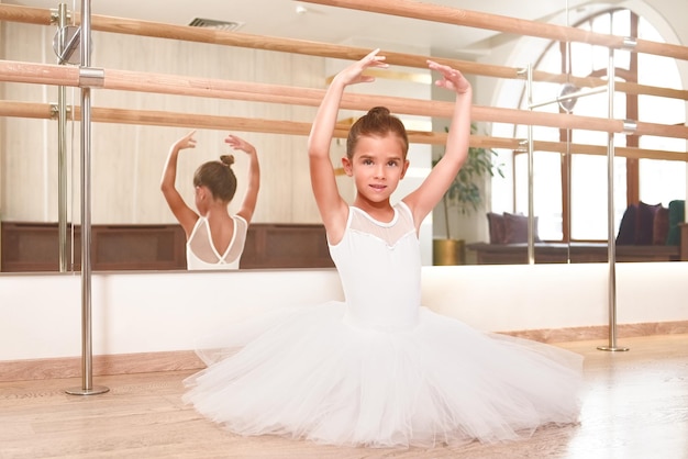 Portret van een schattige kleine ballerina die met haar handen omhoog staat in een performance-jurk ze droomt ervan een professionele balletdanser te worden dansschool balletstudio