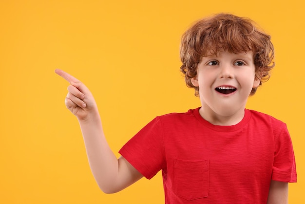 Portret van een schattige kleine jongen die naar iets op een oranje achtergrond wijst