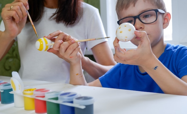 Portret van een schattige kleine jongen die paaseieren schildert met zijn moeder.