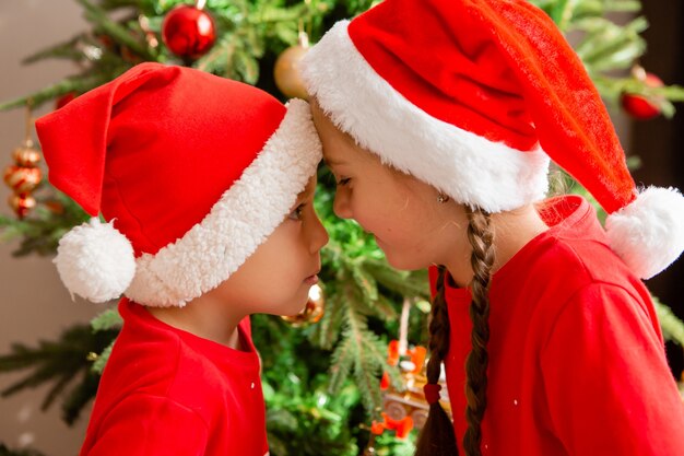 portret van een schattige kleine jongen en meisje in rode pyjama's op de achtergrond van een kerstboom winter